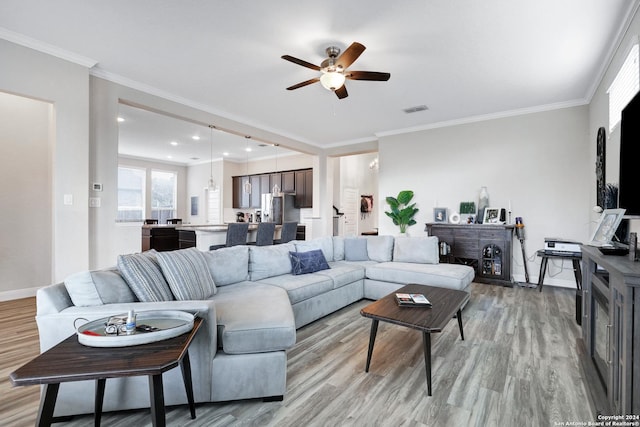 living area with baseboards, visible vents, crown molding, and light wood finished floors