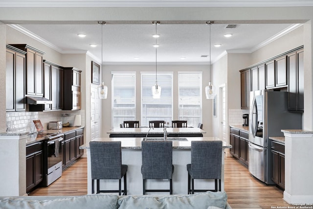 kitchen featuring appliances with stainless steel finishes, light wood-type flooring, under cabinet range hood, and an island with sink