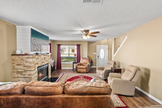 living room with visible vents, a textured ceiling, a stone fireplace, wood finished floors, and baseboards