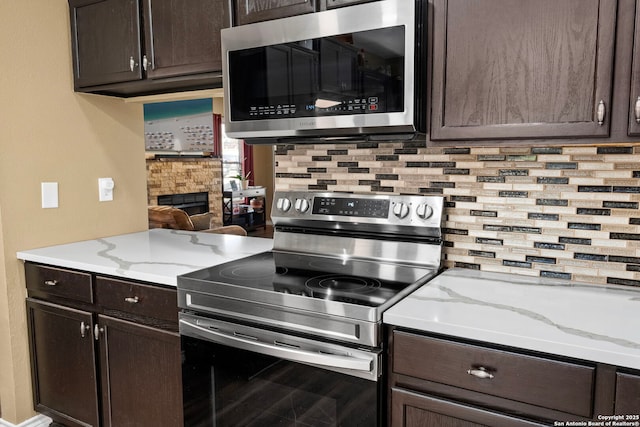 kitchen with dark brown cabinetry, a fireplace, appliances with stainless steel finishes, and backsplash