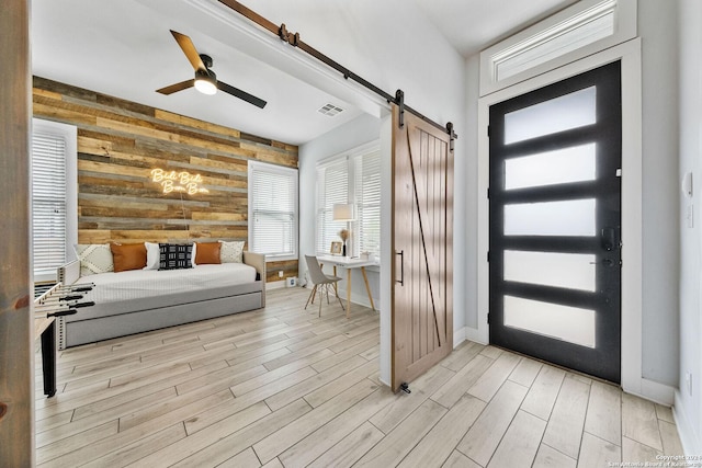 entrance foyer with a barn door, wooden walls, visible vents, ceiling fan, and wood tiled floor