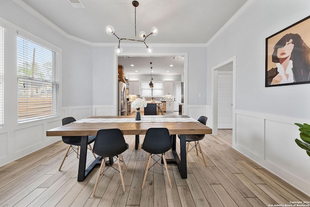 dining area with a wainscoted wall, ornamental molding, a notable chandelier, and light wood-style floors