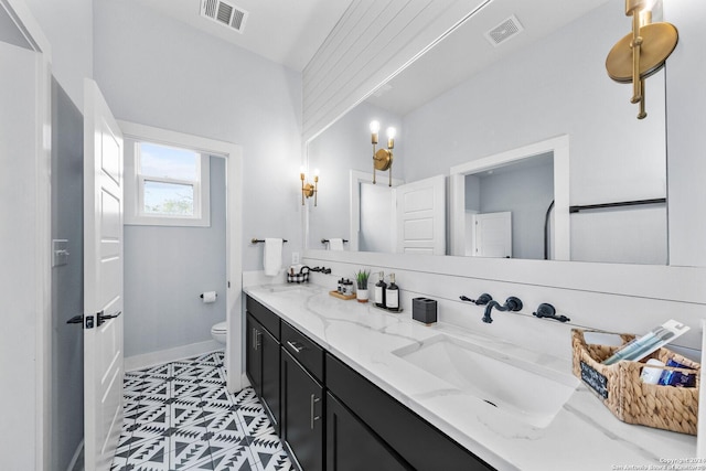 bathroom with toilet, double vanity, visible vents, and a sink