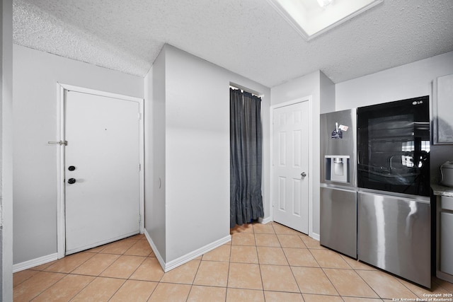 kitchen featuring light tile patterned floors, a textured ceiling, stainless steel refrigerator with ice dispenser, and baseboards