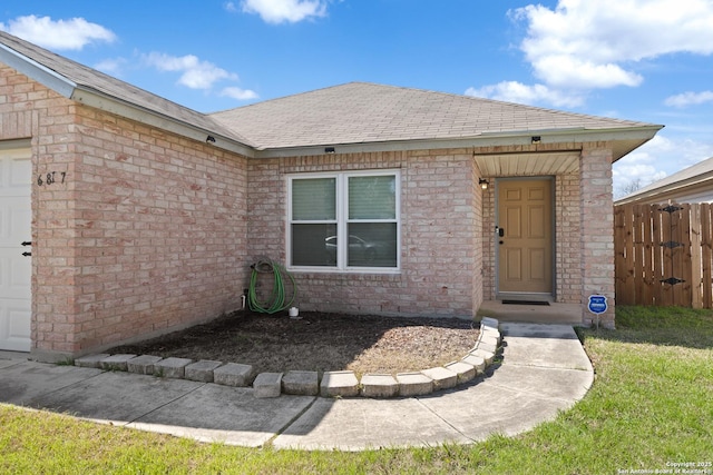 property entrance with a garage, roof with shingles, fence, and brick siding