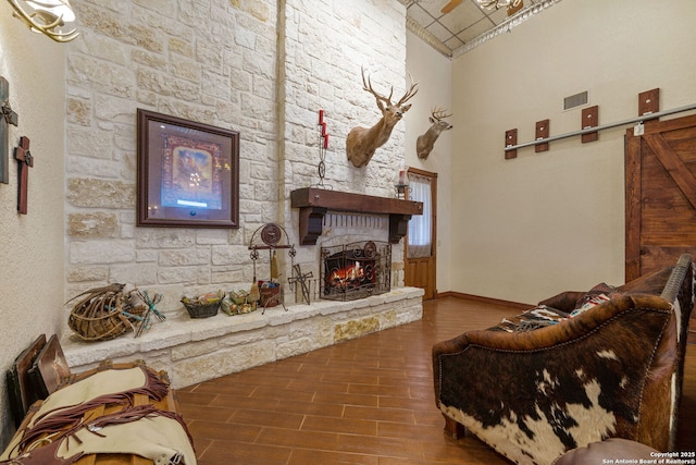 living room with a stone fireplace, a high ceiling, wood finished floors, visible vents, and baseboards