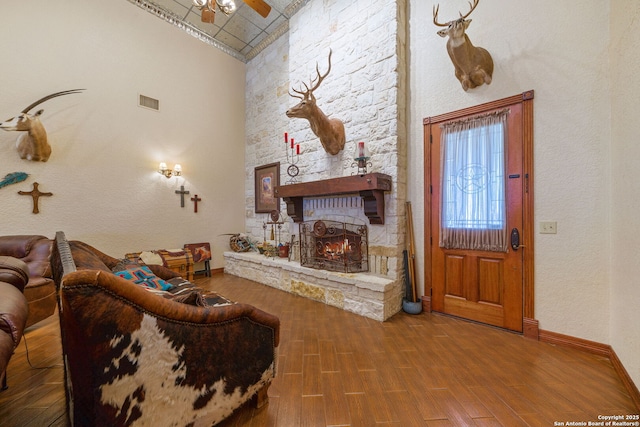 living room with baseboards, a towering ceiling, ceiling fan, wood finished floors, and a fireplace