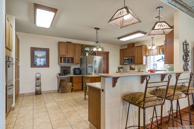 kitchen with appliances with stainless steel finishes, light countertops, brown cabinetry, and a peninsula