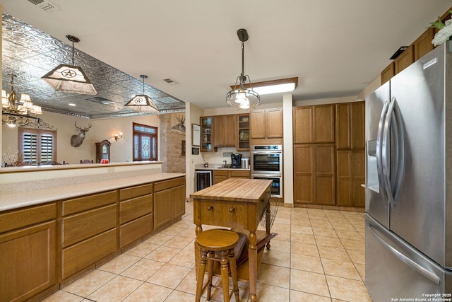 kitchen with light tile patterned floors, butcher block counters, appliances with stainless steel finishes, and brown cabinetry