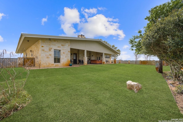 rear view of property with stone siding, a fenced backyard, a yard, and a patio