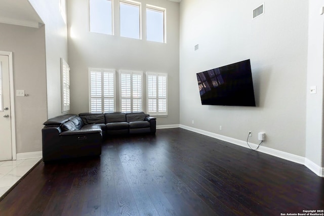 living room featuring visible vents, a high ceiling, baseboards, and wood finished floors