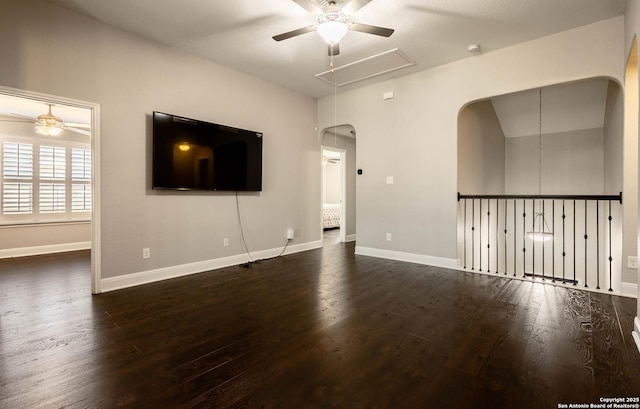 unfurnished living room featuring ceiling fan, dark wood-style flooring, attic access, and baseboards