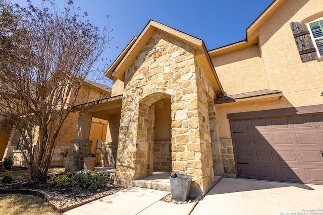 doorway to property with a garage, stone siding, concrete driveway, and stucco siding