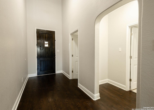 foyer with arched walkways, dark wood finished floors, and baseboards