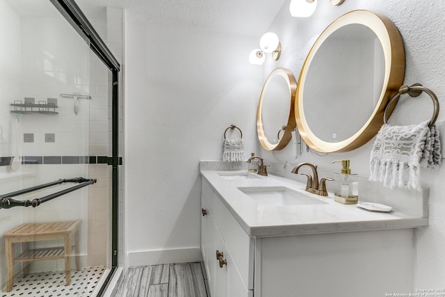 bathroom featuring a stall shower, a sink, baseboards, and double vanity