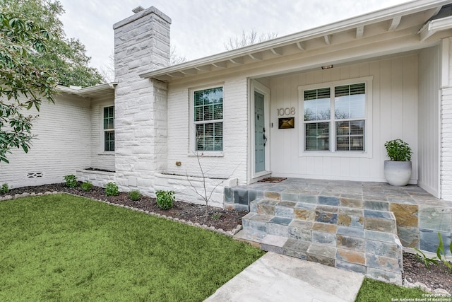 property entrance with covered porch, brick siding, a lawn, board and batten siding, and a chimney