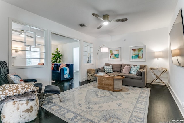 living room featuring dark wood-style floors, visible vents, a ceiling fan, and baseboards