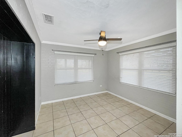 spare room featuring a ceiling fan, visible vents, crown molding, and brick wall