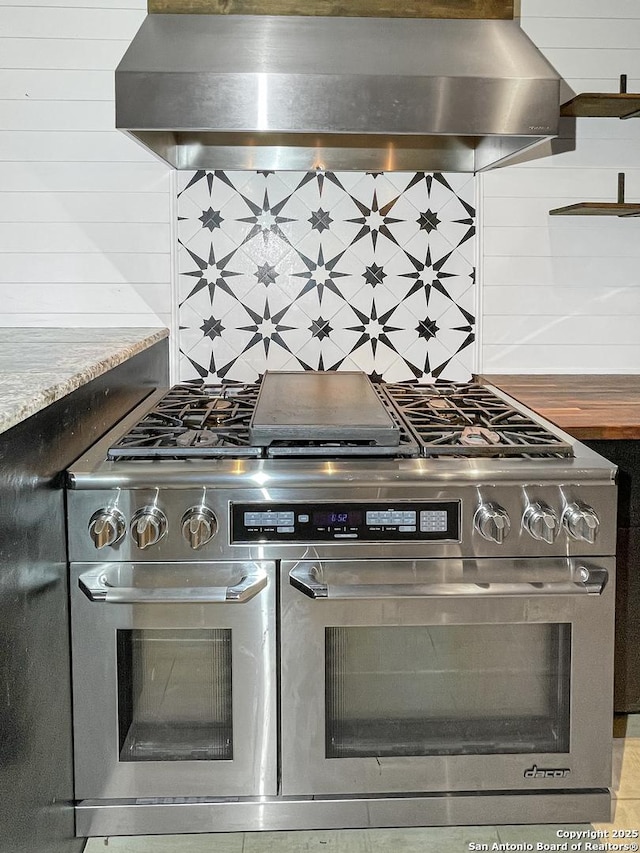 kitchen featuring double oven range, backsplash, and wall chimney exhaust hood