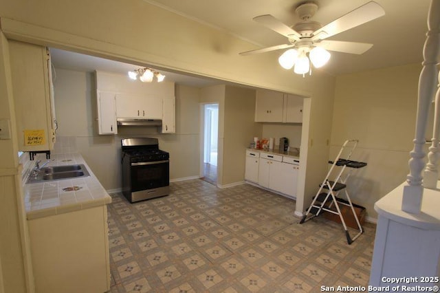 kitchen with under cabinet range hood, a sink, white cabinets, tile counters, and stainless steel range with gas stovetop