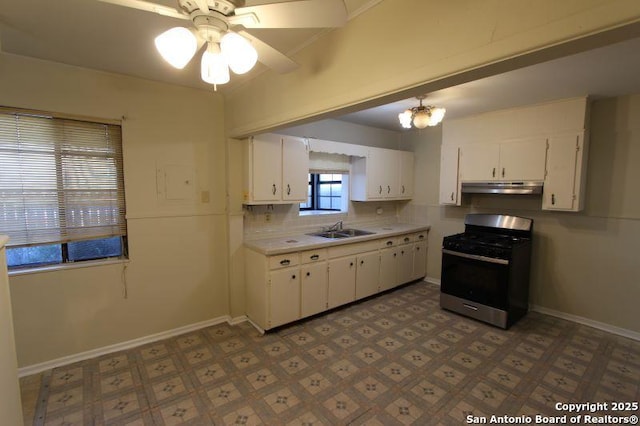 kitchen featuring under cabinet range hood, a sink, white cabinets, light countertops, and gas stove