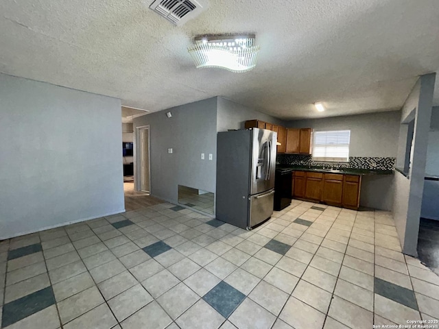 kitchen with light tile patterned flooring, visible vents, stainless steel fridge with ice dispenser, brown cabinetry, and dark countertops