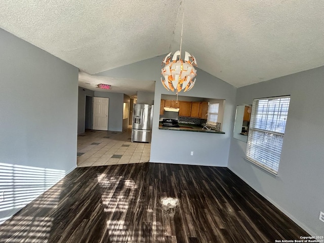 interior space featuring brown cabinetry, dark countertops, wood finished floors, under cabinet range hood, and stainless steel refrigerator with ice dispenser