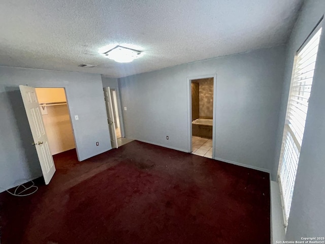 unfurnished bedroom featuring a textured ceiling, connected bathroom, visible vents, carpet, and a walk in closet