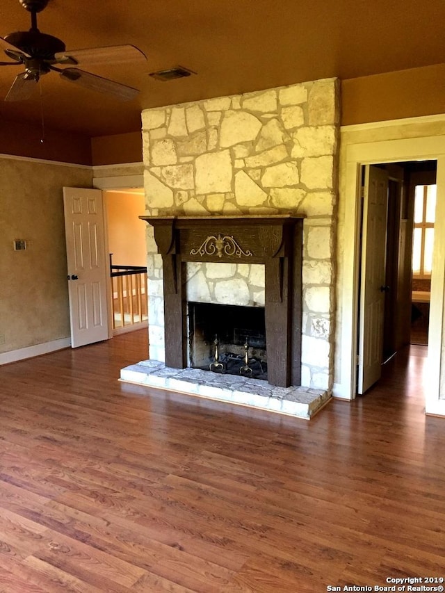 unfurnished living room featuring ceiling fan, a stone fireplace, wood finished floors, and visible vents