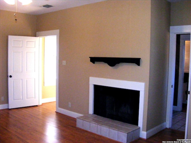 interior details featuring baseboards, visible vents, a tiled fireplace, and wood finished floors