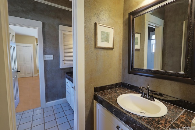 bathroom with a textured wall, tile patterned flooring, vanity, and baseboards