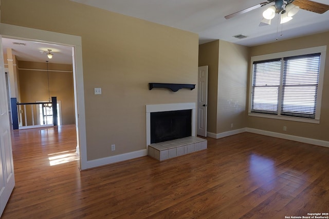 unfurnished living room featuring ceiling fan, wood finished floors, visible vents, baseboards, and a tiled fireplace