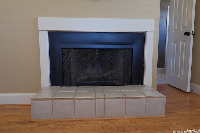 room details featuring a fireplace with raised hearth, wood finished floors, and baseboards