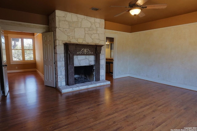 unfurnished living room featuring a ceiling fan, visible vents, dark wood finished floors, and a stone fireplace