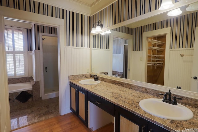 bathroom with a shower stall, wainscoting, a sink, and wallpapered walls