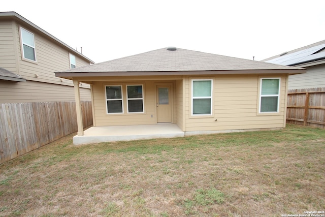 back of property with roof with shingles, a fenced backyard, a patio, and a lawn