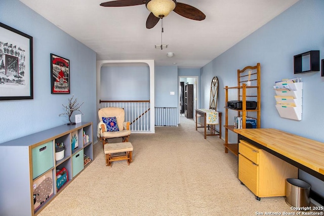 living area with a ceiling fan, light carpet, and an upstairs landing