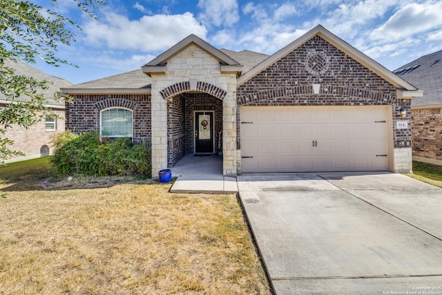 french country home with a garage, brick siding, concrete driveway, stone siding, and a front yard