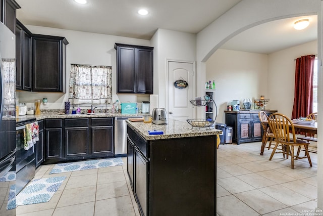 kitchen with arched walkways, light tile patterned flooring, light stone countertops, a center island, and dishwasher