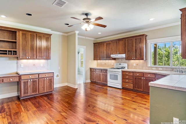 kitchen with wood finished floors, under cabinet range hood, white range with gas cooktop, a sink, and visible vents
