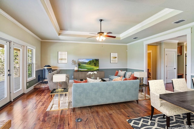 living room featuring a raised ceiling, visible vents, ornamental molding, wood finished floors, and a ceiling fan
