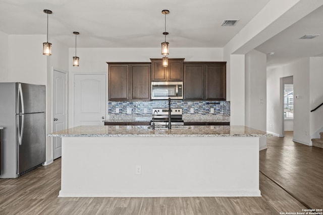 kitchen featuring light wood-style floors, a center island with sink, light stone counters, and stainless steel appliances