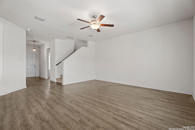 unfurnished room featuring visible vents, a ceiling fan, wood finished floors, baseboards, and stairs