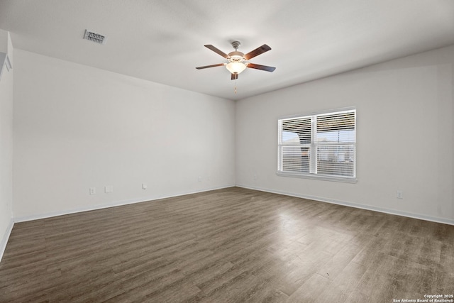 spare room with a ceiling fan, visible vents, dark wood finished floors, and baseboards