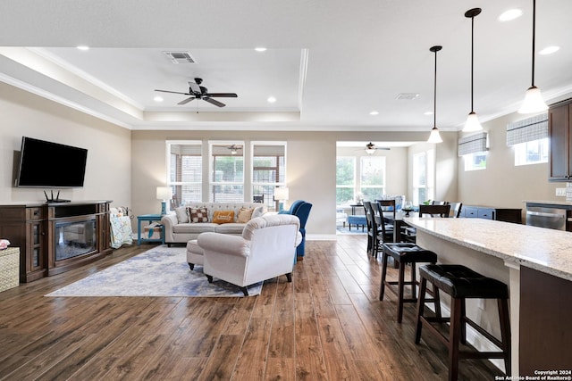 living area featuring recessed lighting, dark wood-type flooring, visible vents, a raised ceiling, and crown molding