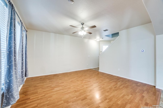 empty room featuring light wood-style floors, ceiling fan, stairs, and visible vents