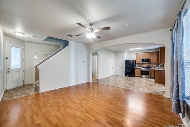 unfurnished living room with arched walkways, ceiling fan, light wood finished floors, and stairs