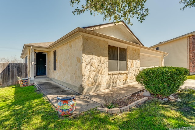 view of side of home featuring an attached garage, stone siding, fence, and a lawn