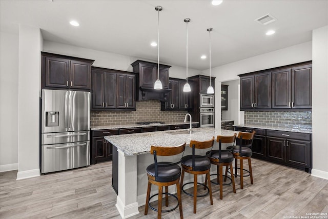 kitchen featuring stainless steel appliances, a sink, visible vents, light wood finished floors, and a kitchen bar