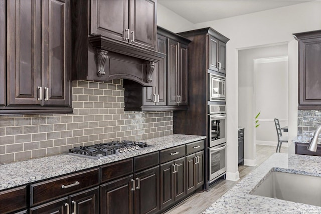 kitchen featuring backsplash, light stone counters, stainless steel appliances, and a sink